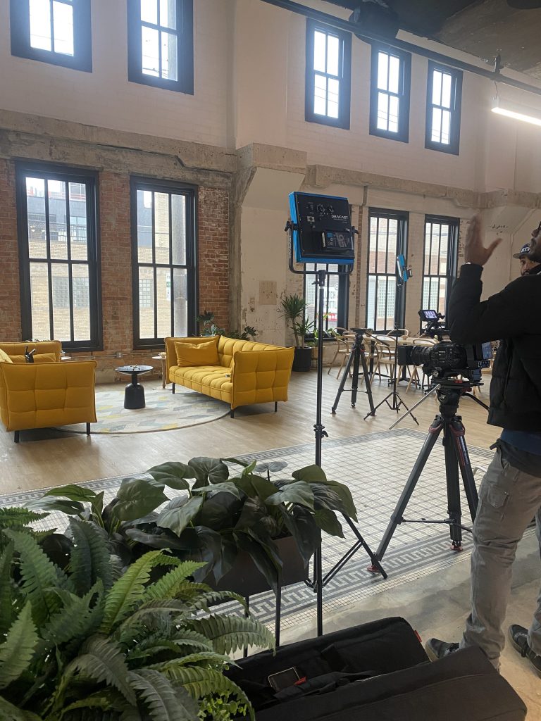Image of coworking space with yellow couches, an exposed brick wall, and filming equipment.