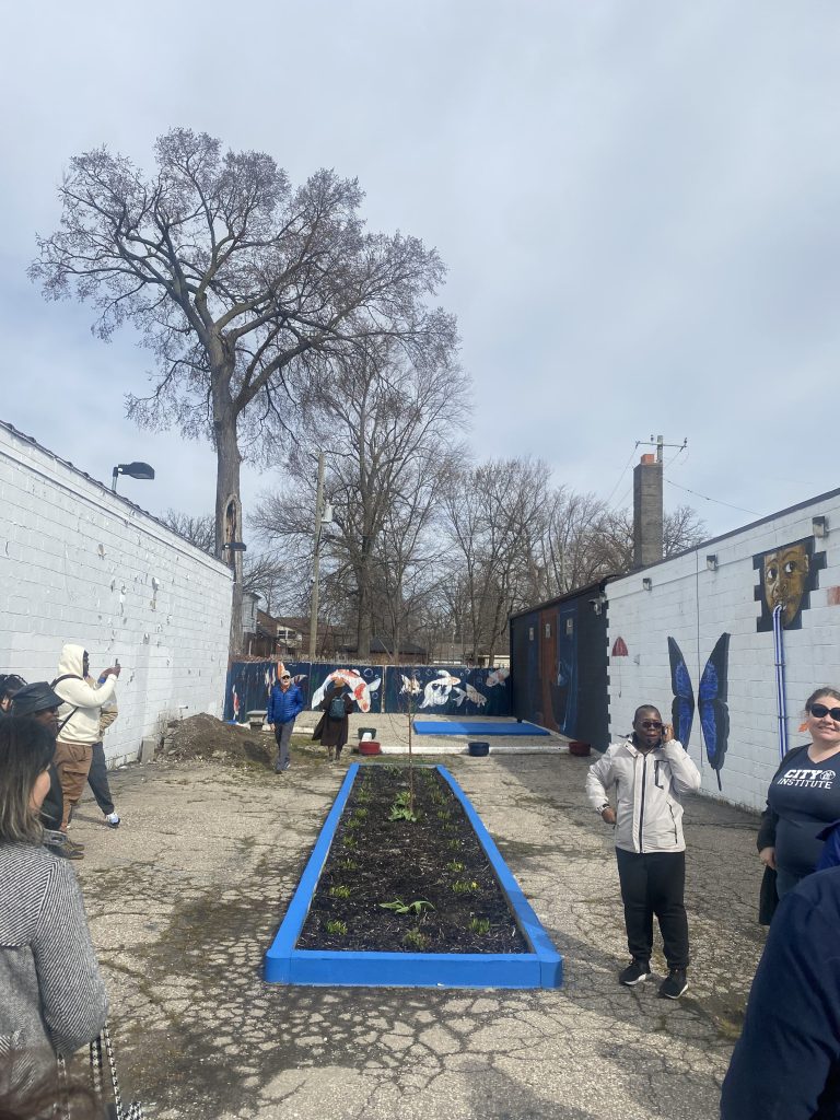 Image of outdoor space with people gathered around a raised garden bed with bright blue borders.